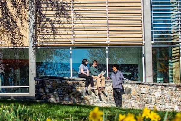 Three students sitting on a rock wall outside of Rhoades Robinson Hall